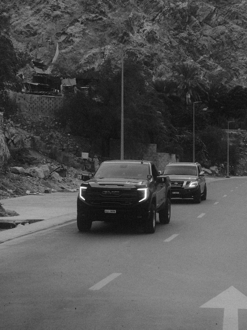 Two black SUVs driving on a winding road surrounded by trees and rocky terrain.