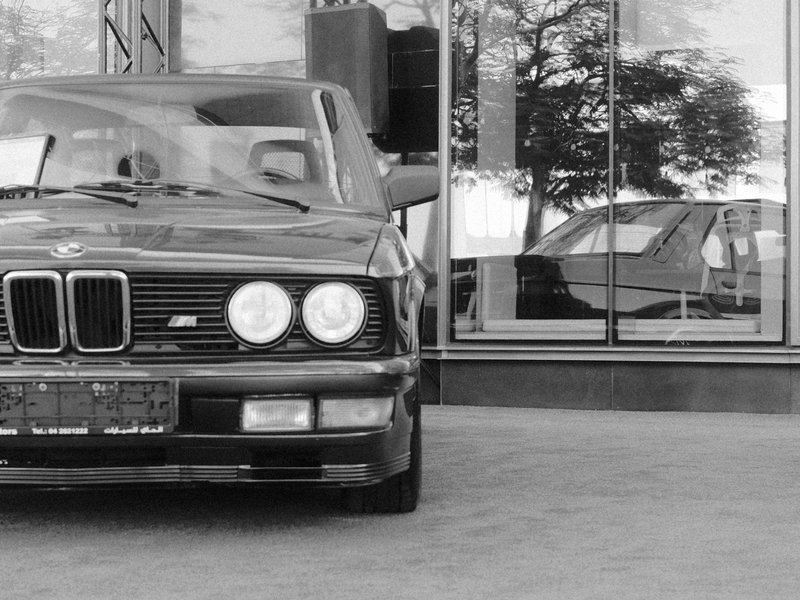A classic black BMW car parked in front of a reflective glass building, showcasing its sleek design.