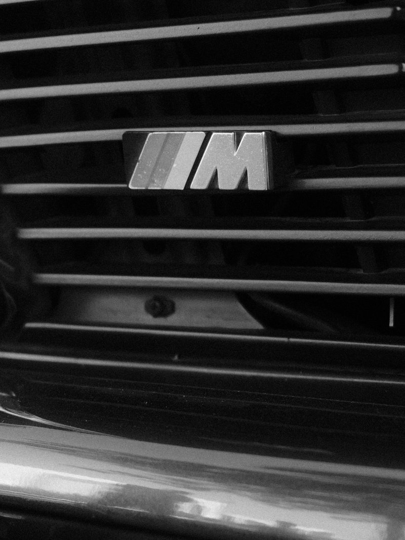 Close-up of a car's grille featuring the BMW M logo, with horizontal slats in the background.