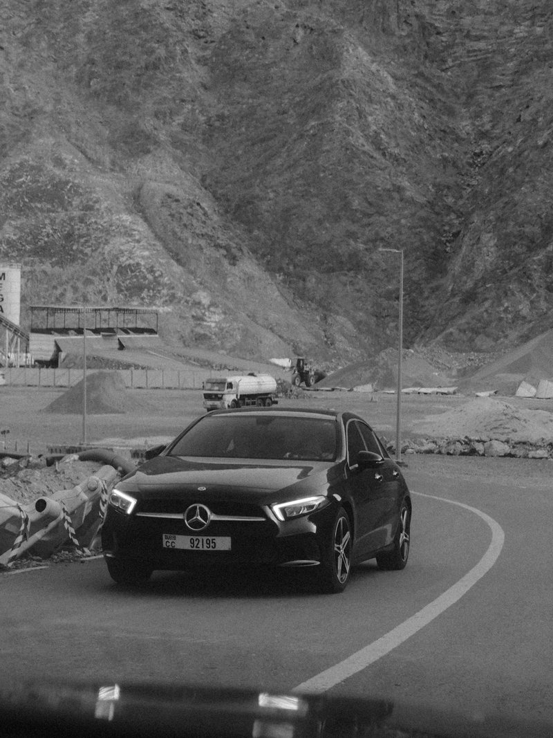 A black Mercedes-Benz car driving on a winding road with rocky mountains in the background.