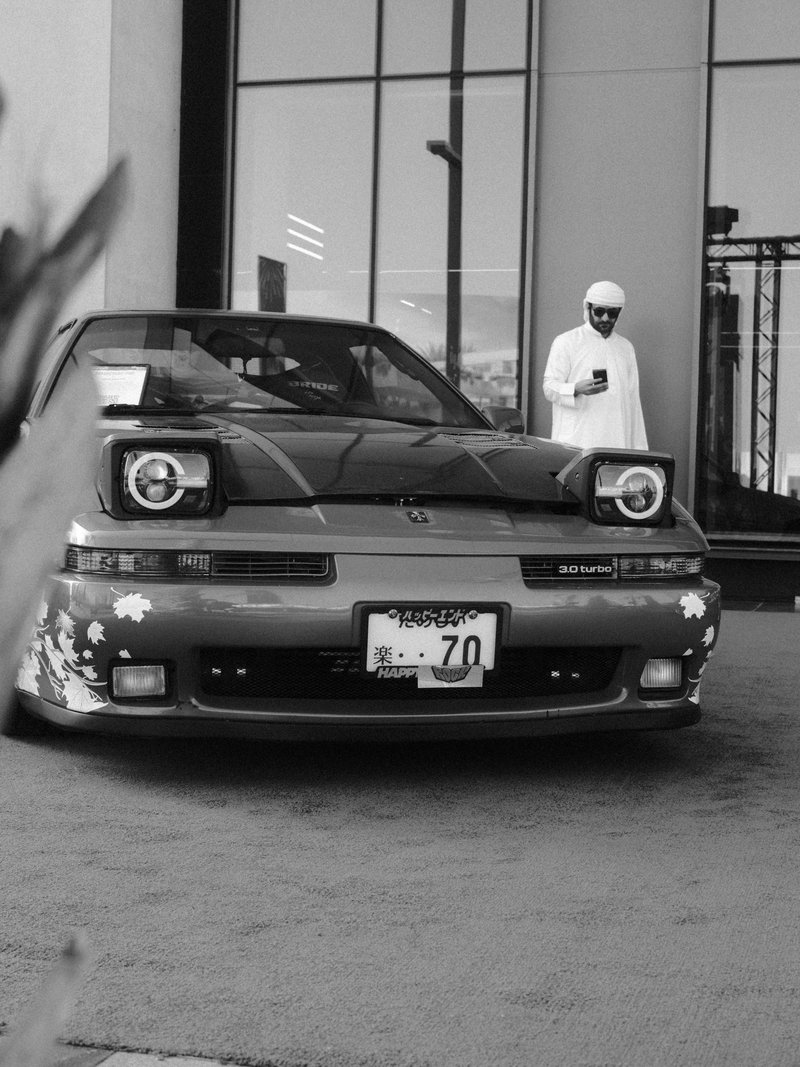 A modified car parked in front of a building with a person in traditional attire standing nearby.
