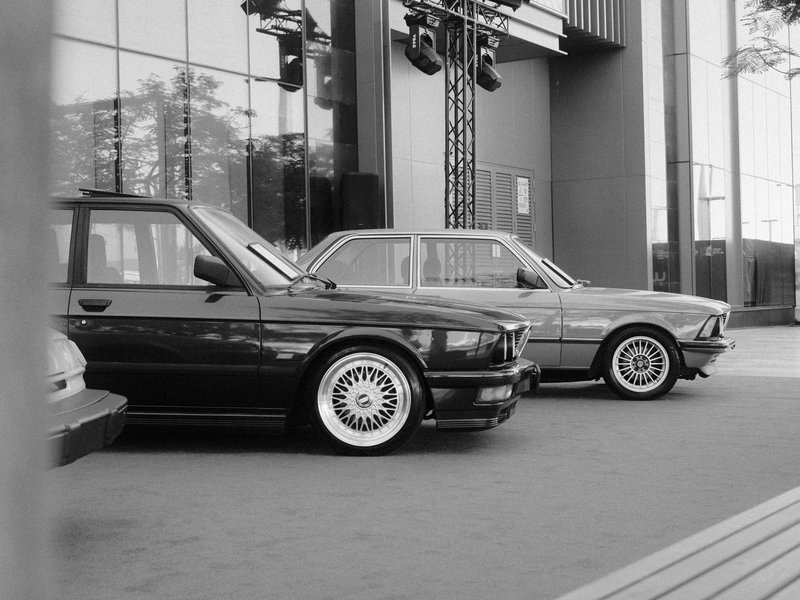 Two classic cars parked in front of a modern building, showcasing vintage design against contemporary architecture.