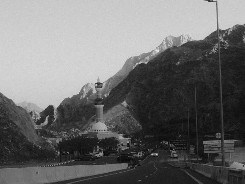 A mountainous landscape with a road leading towards a tower and buildings in the foreground.