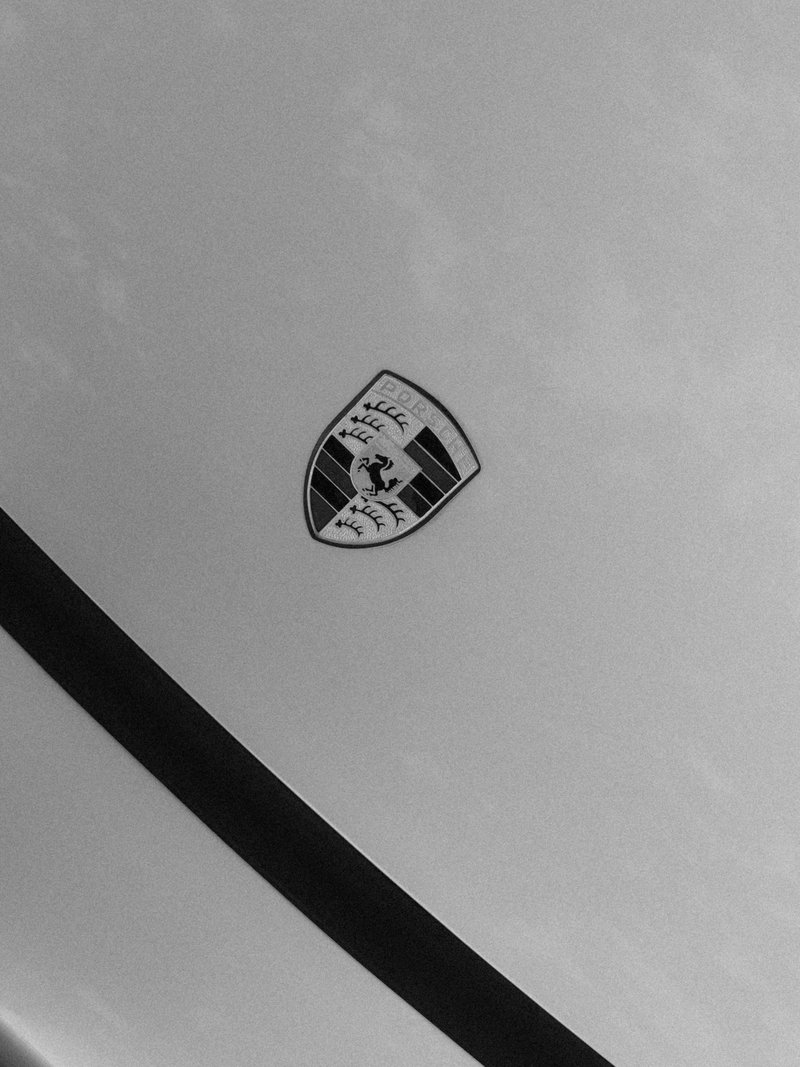Close-up of a Porsche emblem on a silver car surface, highlighting the logo's details.