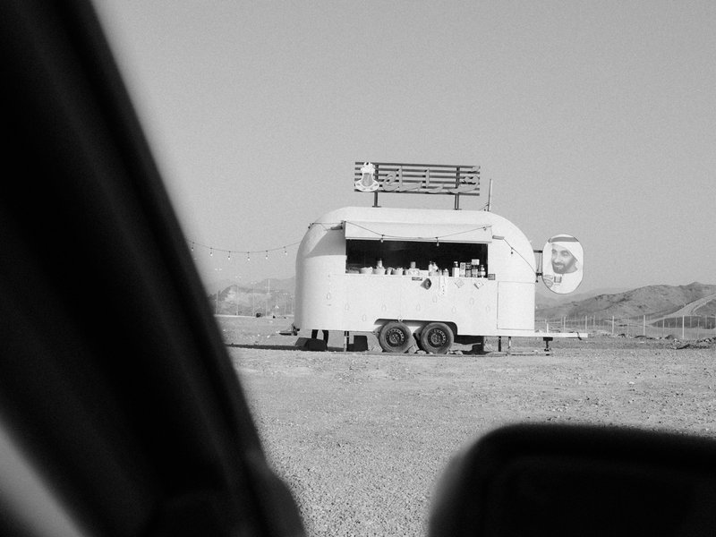 A food truck in a desolate landscape, captured from a car window, with mountains in the background.