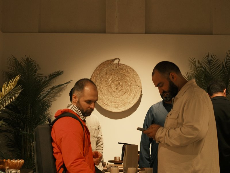 Two men in a cozy indoor setting, one in an orange jacket and the other with a beard, engaged in conversation.