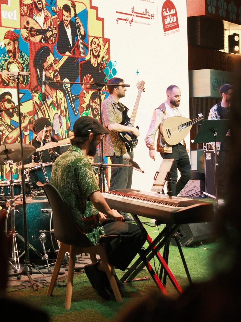 A live band performing on stage with colorful backdrop and instruments including keyboard, guitar, and drums.