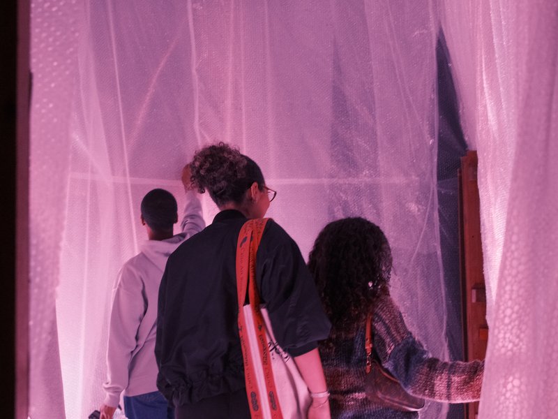 Three people walking through a sheer pink curtain in a dimly lit space.