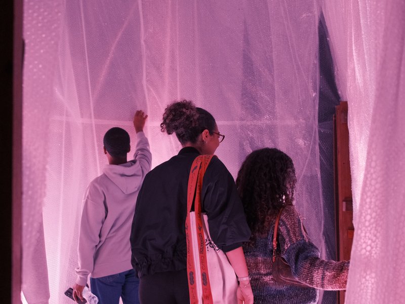 Three individuals interacting with translucent fabric in a softly lit space, creating a dreamy atmosphere.