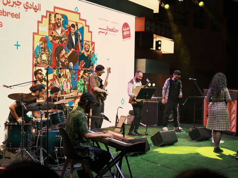 A live band performing on stage with colorful backdrop and audience in a lively atmosphere.
