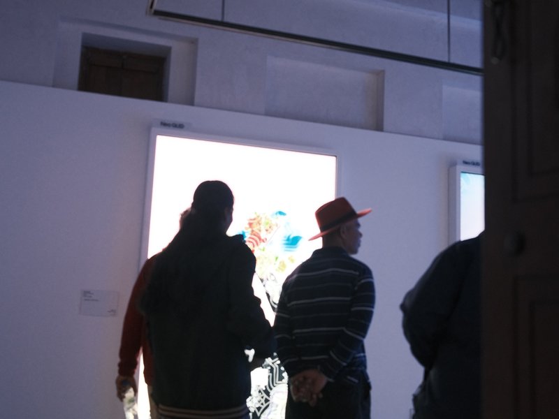 Silhouettes of people viewing art in a gallery with bright artwork illuminated in the background.
