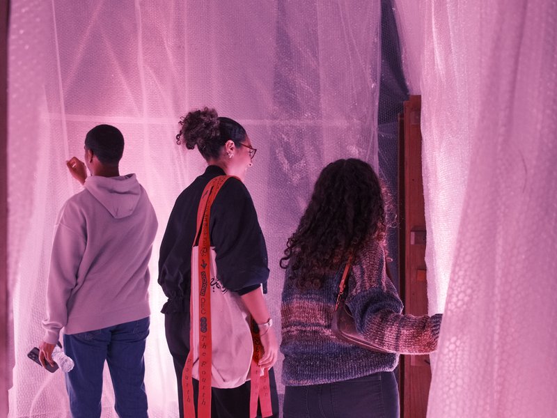 Three individuals interacting with a translucent curtain in a softly lit space.