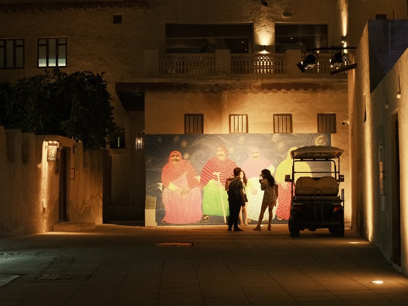 Two women interacting in front of a colorful mural at night, with a golf cart nearby.
