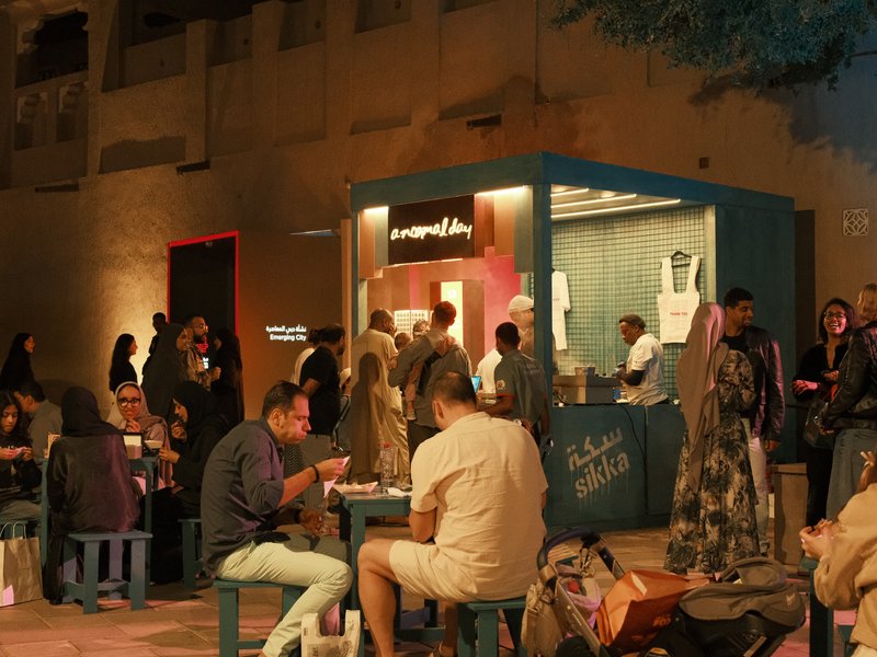A bustling outdoor food market scene with people dining and a food stall illuminated at night.