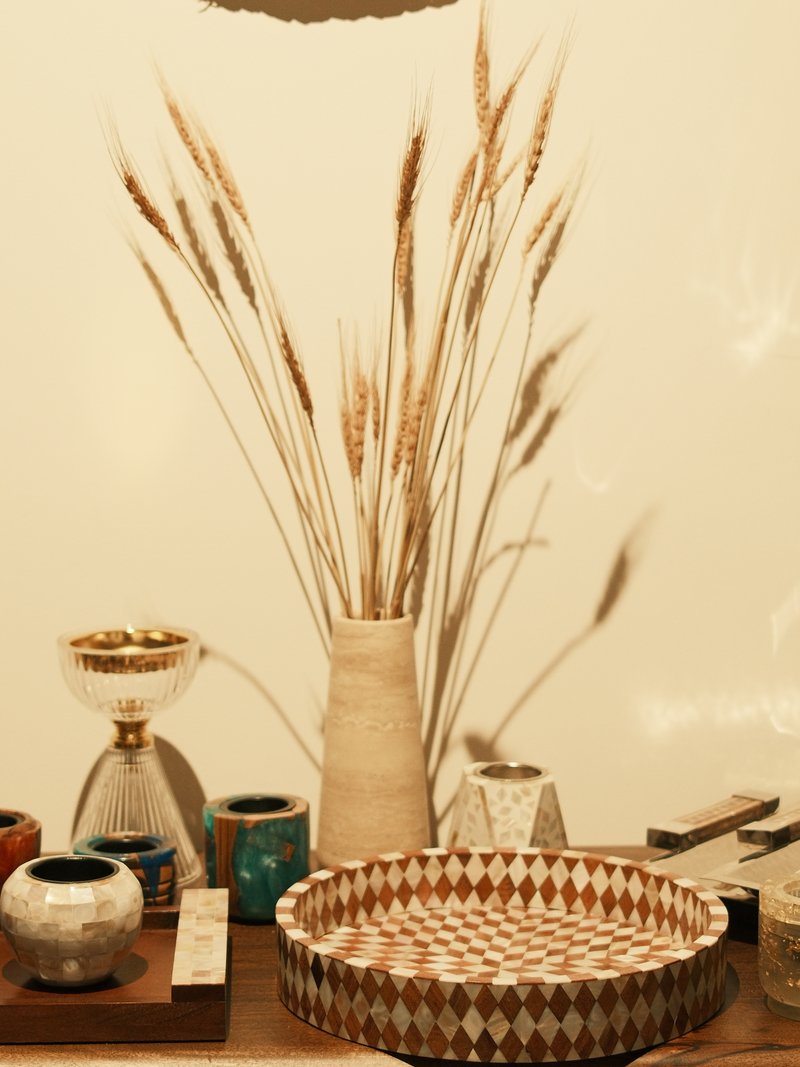 A still-life arrangement featuring decorative vases and dried wheat in a neutral-toned setting.