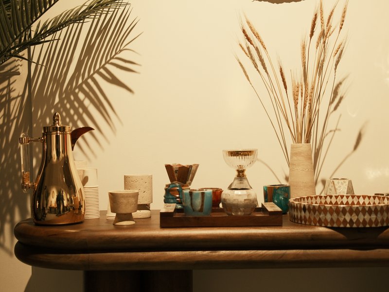 A wooden table displaying various decorative items including a coffee maker, cups, and dried plants.