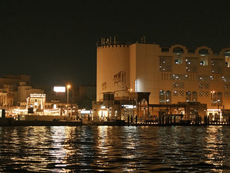 Night view of a waterfront with illuminated buildings and reflections on the water.