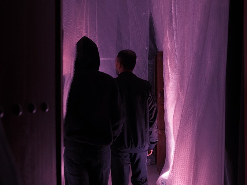 Two figures silhouetted against a translucent curtain, illuminated by soft purple light.