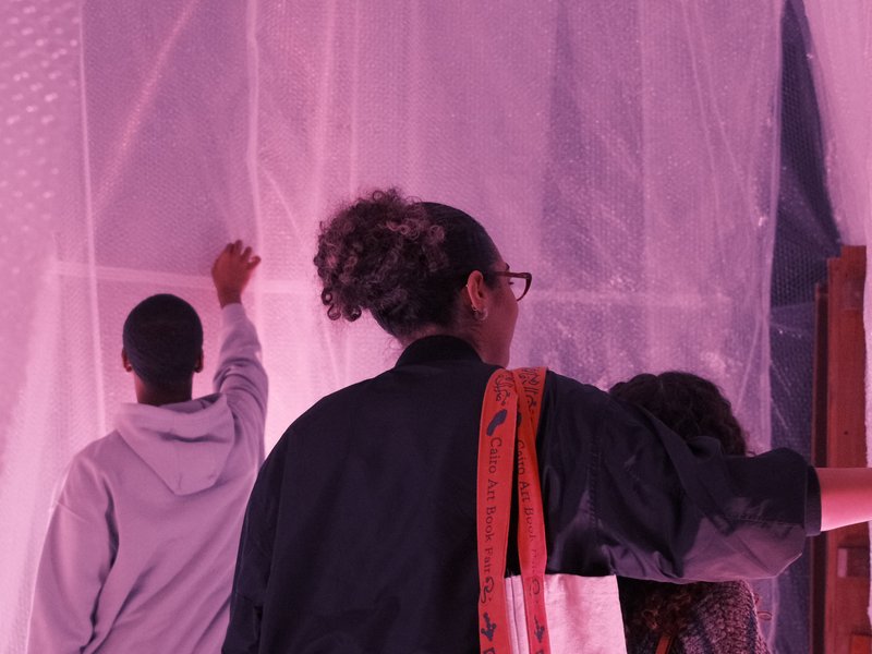 Three individuals interacting with a translucent pink backdrop in an indoor setting.