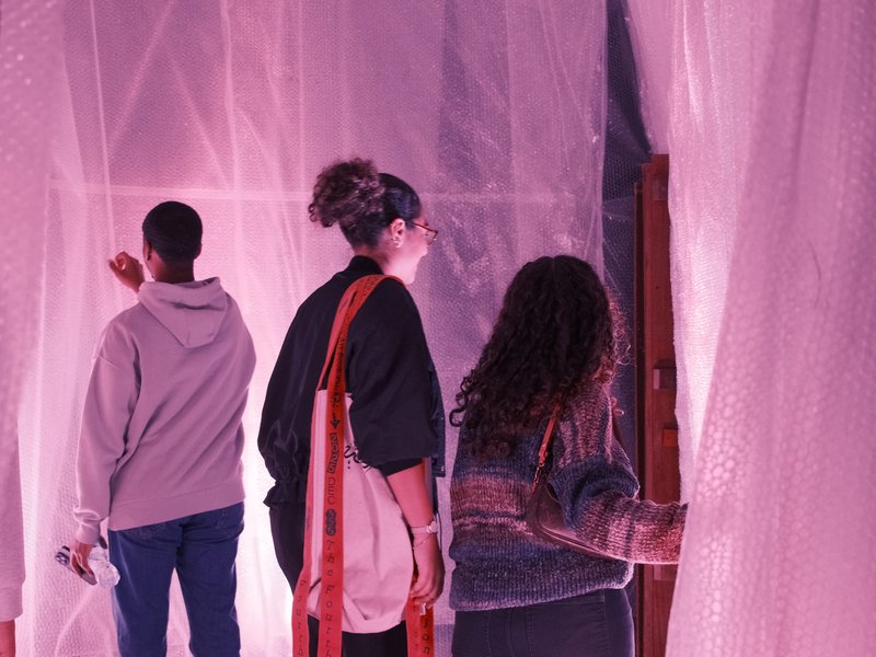 Three people interacting with translucent pink fabric in an indoor space, creating a dreamy atmosphere.