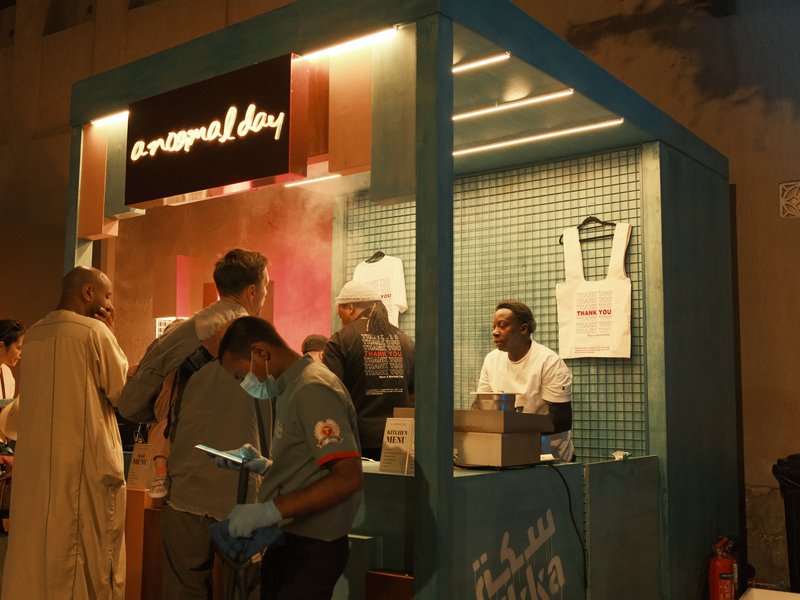A vibrant food stall at night with people interacting and a vendor serving customers.