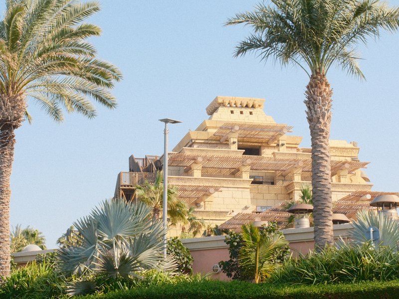 A large pyramid structure surrounded by palm trees and greenery under a clear blue sky.