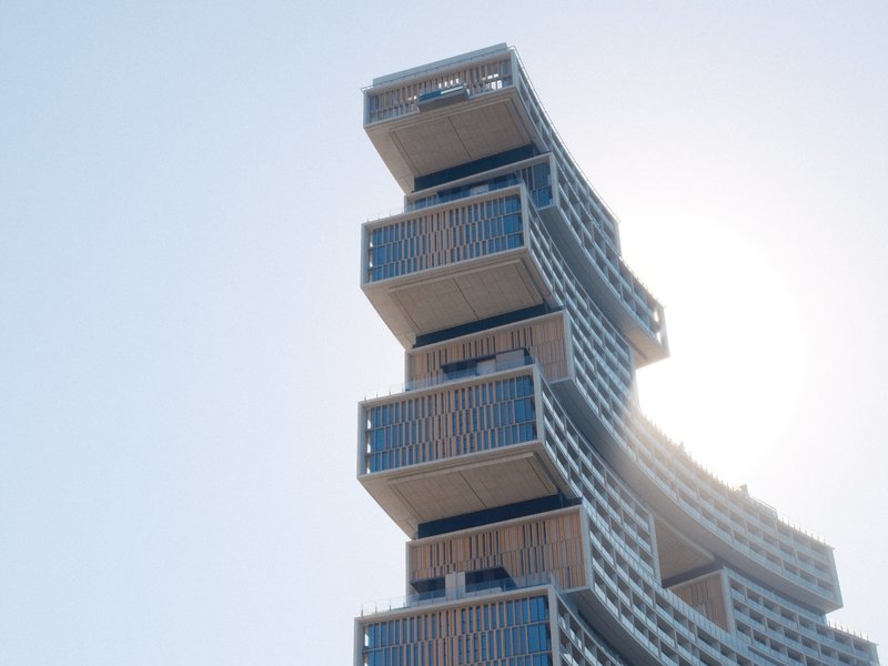 Modern architectural structure with stacked balconies against a clear sky and sunlight.