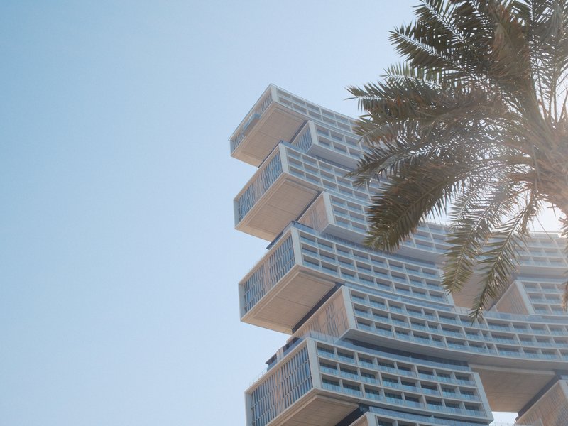 Modern architectural structure with layered design against a clear blue sky and palm tree.