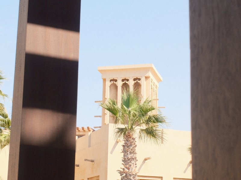 View of a traditional building with a wind tower and palm tree against a clear blue sky.