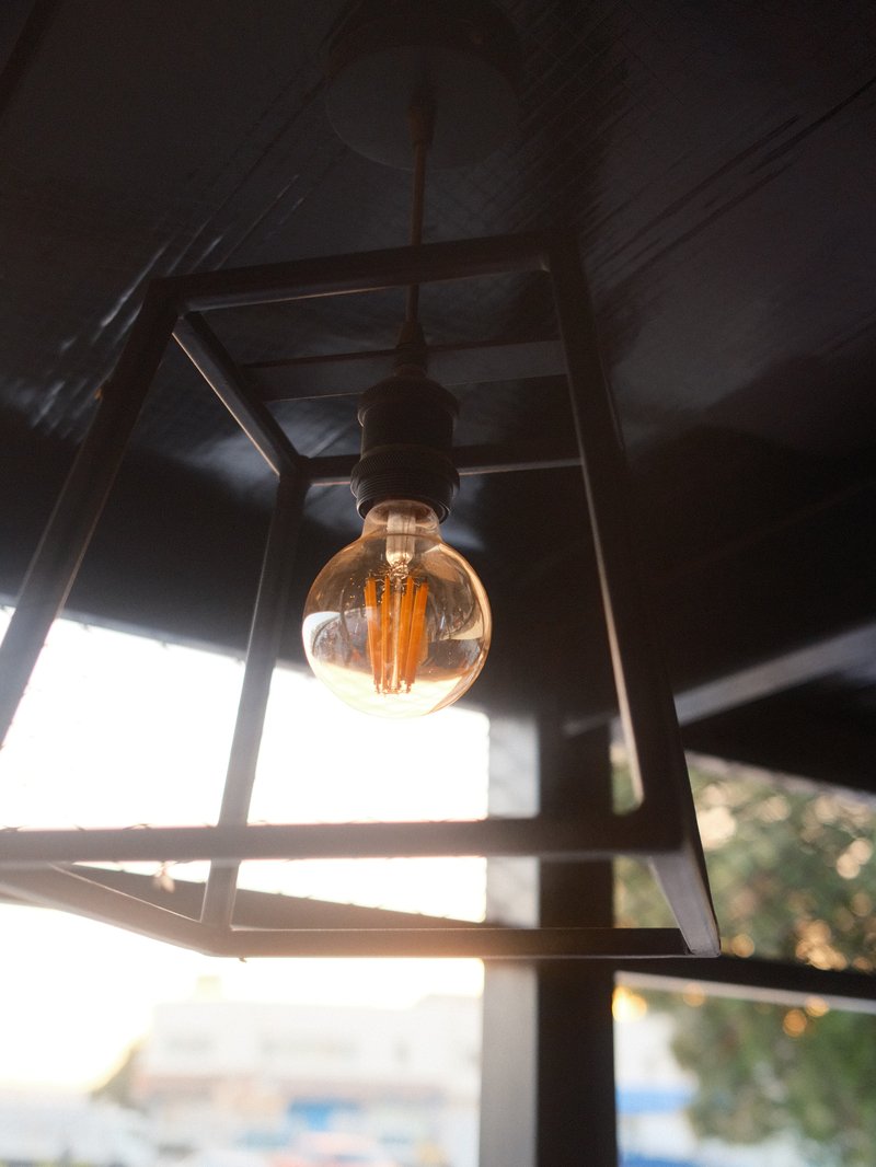 A close-up of a vintage light bulb hanging from a geometric metal fixture against a blurred background.