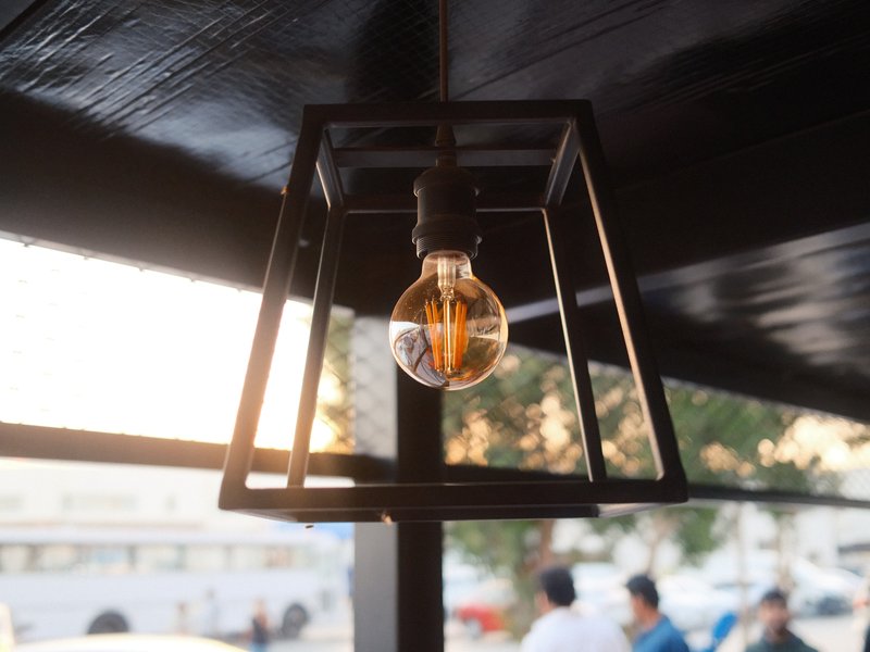 A vintage-style light bulb hanging in a geometric metal frame with a warm glow against a blurred background.
