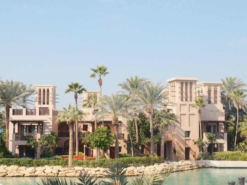 A modern architectural structure with palm trees and a water feature under a clear blue sky.