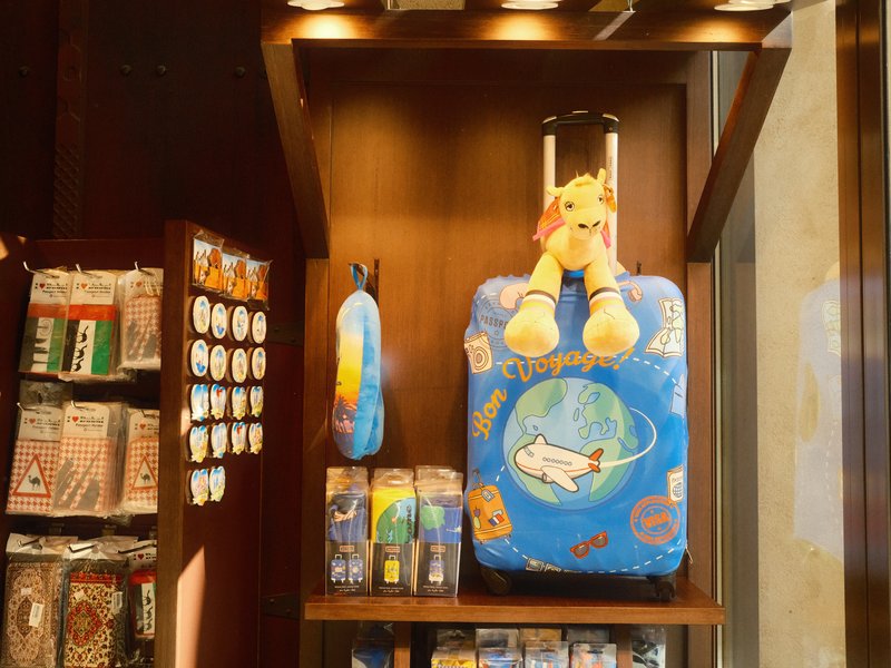 A colorful children's suitcase with a plush toy on top, displayed in a shop with various merchandise.