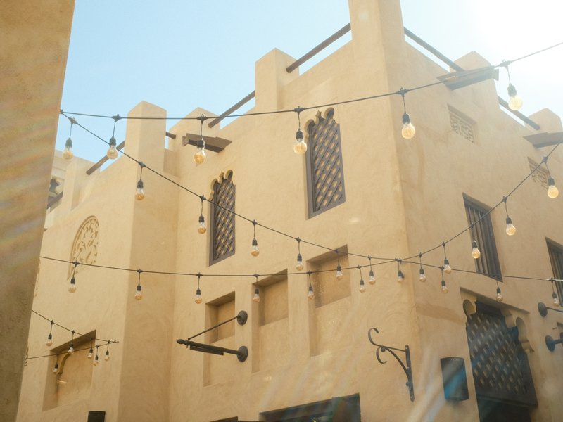 A sunlit building with decorative string lights and architectural details in a warm, sandy color.
