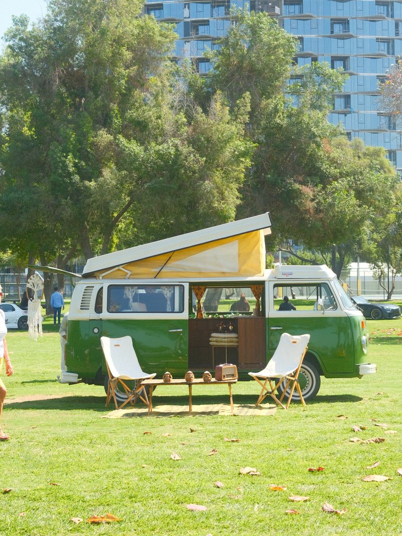 A vintage green camper van with a yellow pop-up roof parked on a grassy area, surrounded by trees.