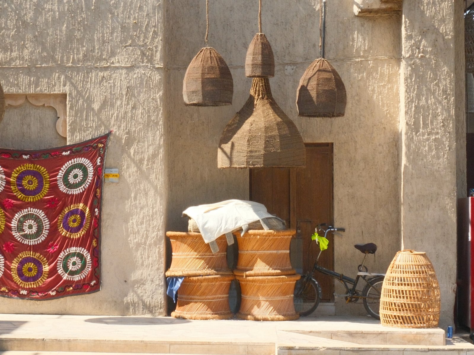 A rustic scene featuring woven baskets, a bicycle, and colorful textiles hanging on a wall.