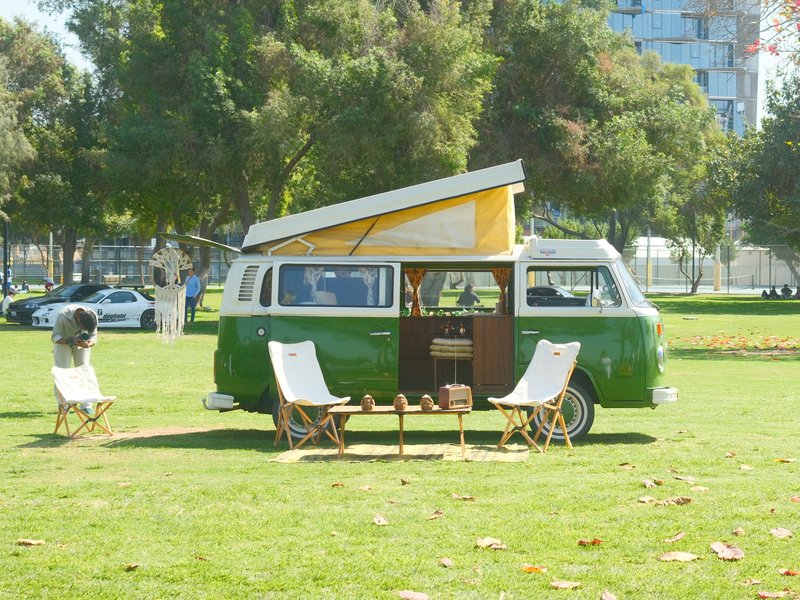 A vintage green camper van parked on grass with chairs and a picnic setup nearby.