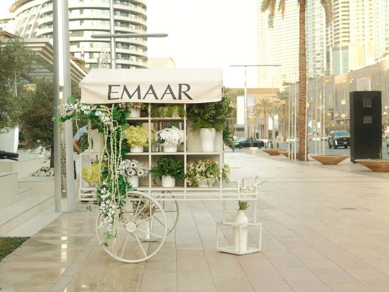 A decorative flower cart with greenery and flowers on a city street, surrounded by modern buildings.