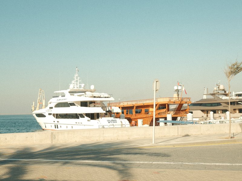A white yacht and an orange boat docked at a marina under a clear sky.