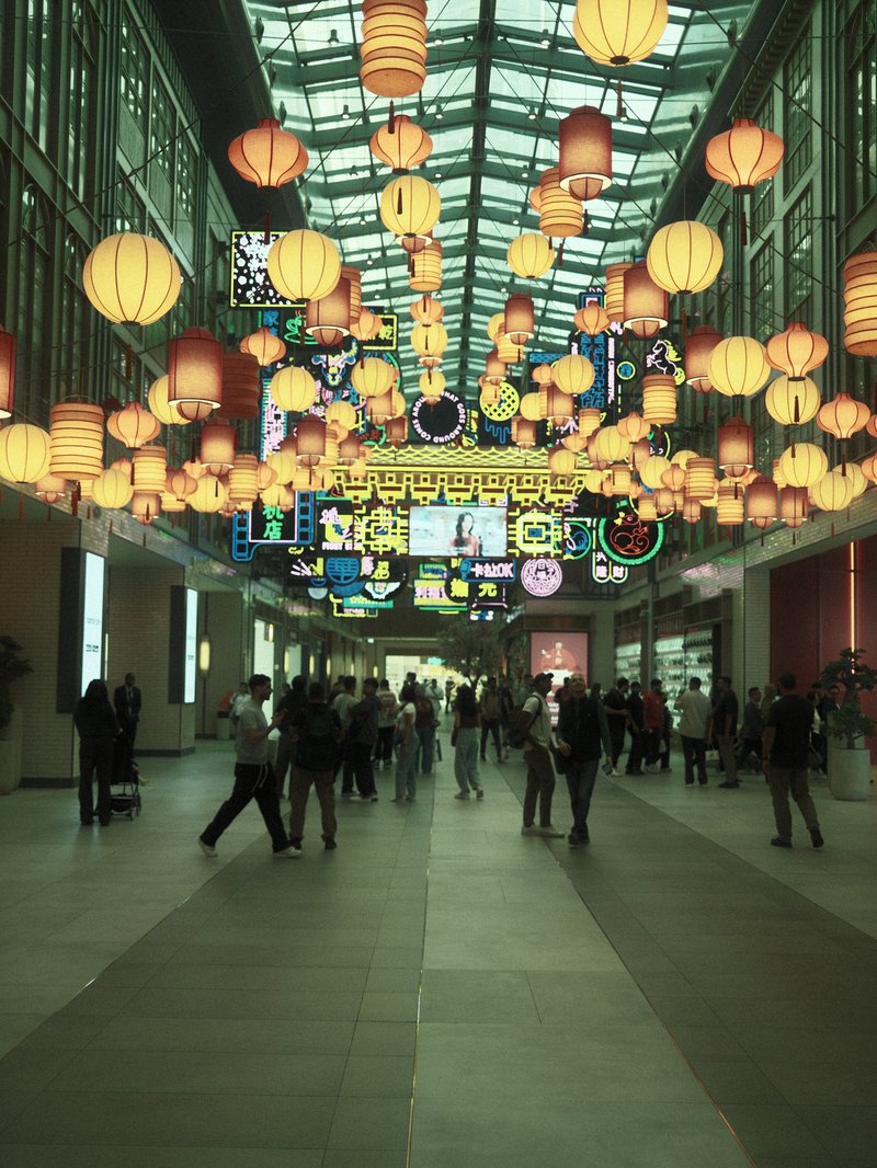 A bustling indoor space filled with colorful lanterns and neon signs, with people walking through.