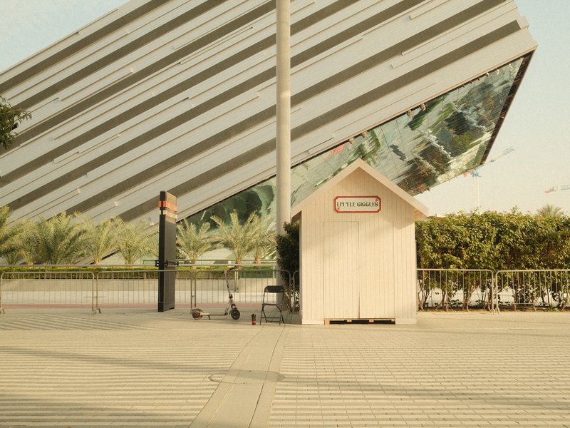 A modern building with a slanted glass facade next to a small white structure resembling a kiosk.