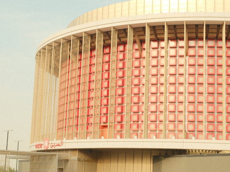 A modern architectural building with a curved facade and red paneling under a pale sky.