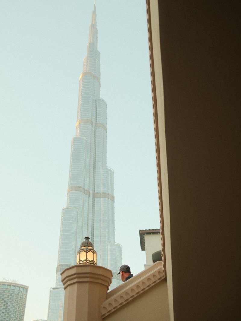 A view of the Burj Khalifa towering above a building, with a person partially visible in the foreground.