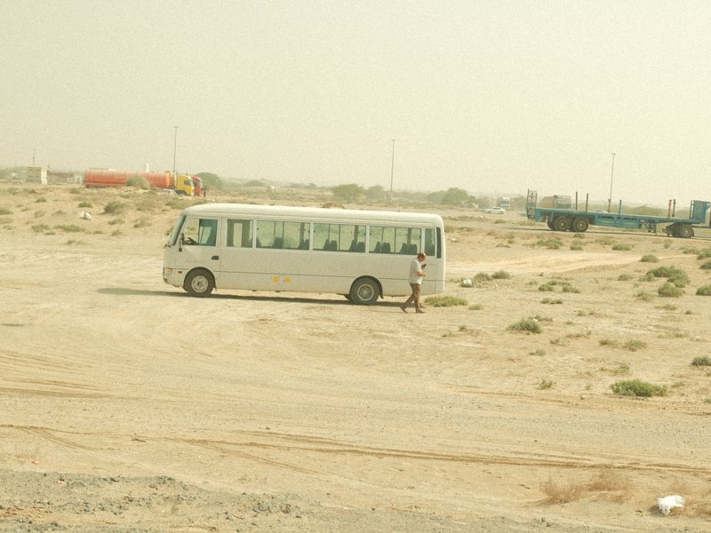 A white bus parked in a barren, dusty landscape with a person standing beside it.