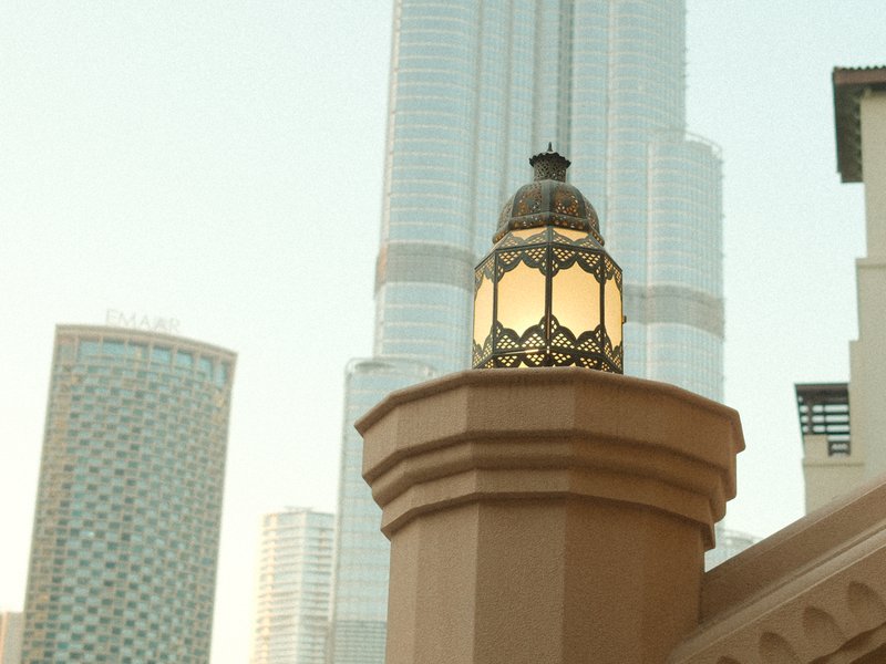 A decorative lantern atop a building with modern skyscrapers in the background during golden hour.