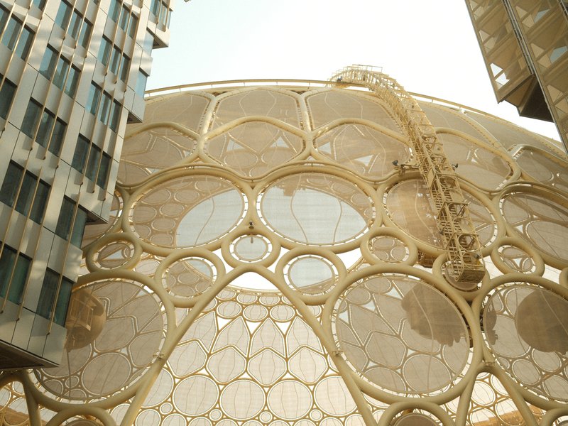 Unique architectural structure with honeycomb design surrounded by modern buildings under bright light.