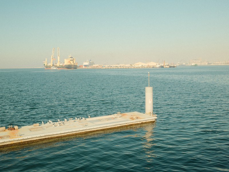 A serene view of a calm sea with a distant harbor and a pier extending into the water.