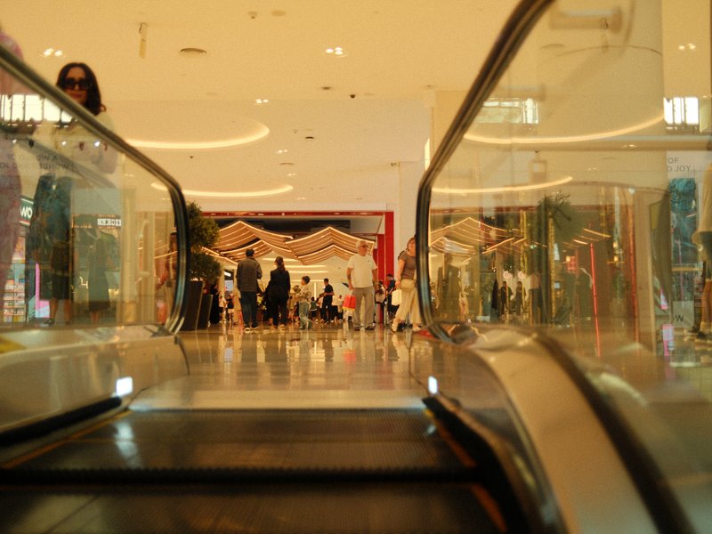 View from an escalator looking towards a busy shopping area with people and decorative elements.
