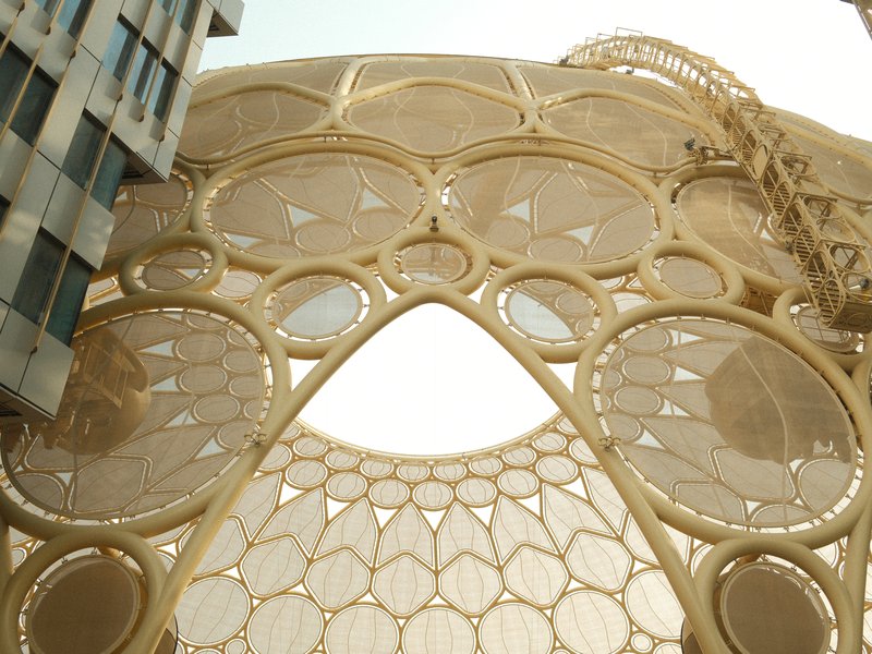 Close-up view of a modern architectural structure with intricate circular designs and a crane in the background.