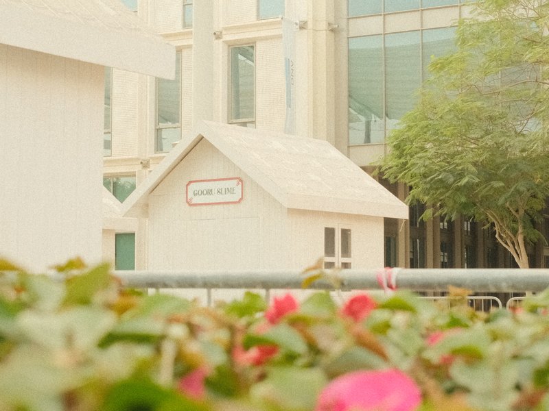A small white house structure surrounded by greenery and flowers in an urban setting.